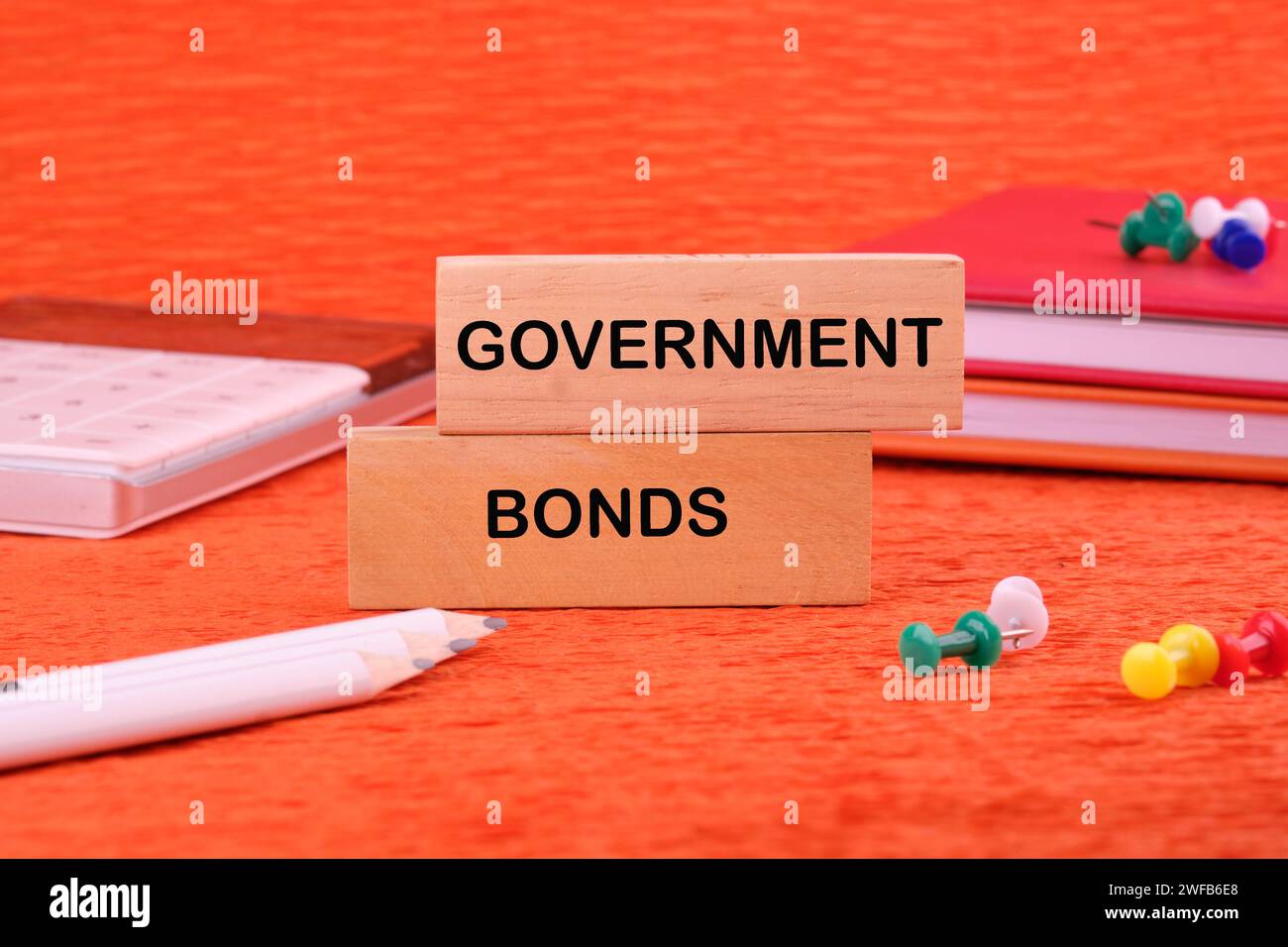 Text von Staatsanleihen auf einem Holzblock auf orangem Hintergrund neben Bürobedarf Stockfoto