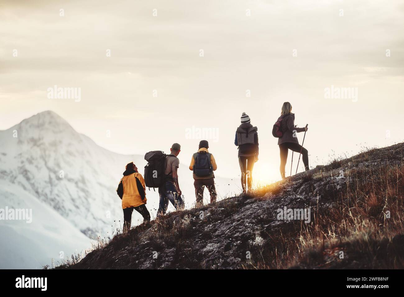 Eine Gruppe von Wanderern aus gemischtem Alter steht am Berghang und sieht den Sonnenuntergang Stockfoto