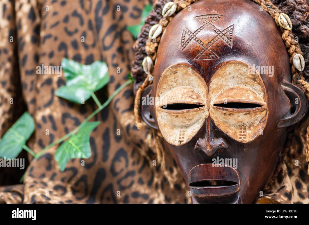 Afrikanische Holzmaske aus Uganda, zum Familien- oder Personenschutz, aus heimischem Holz, Seilen und Muscheln als Haarschmuck Stockfoto