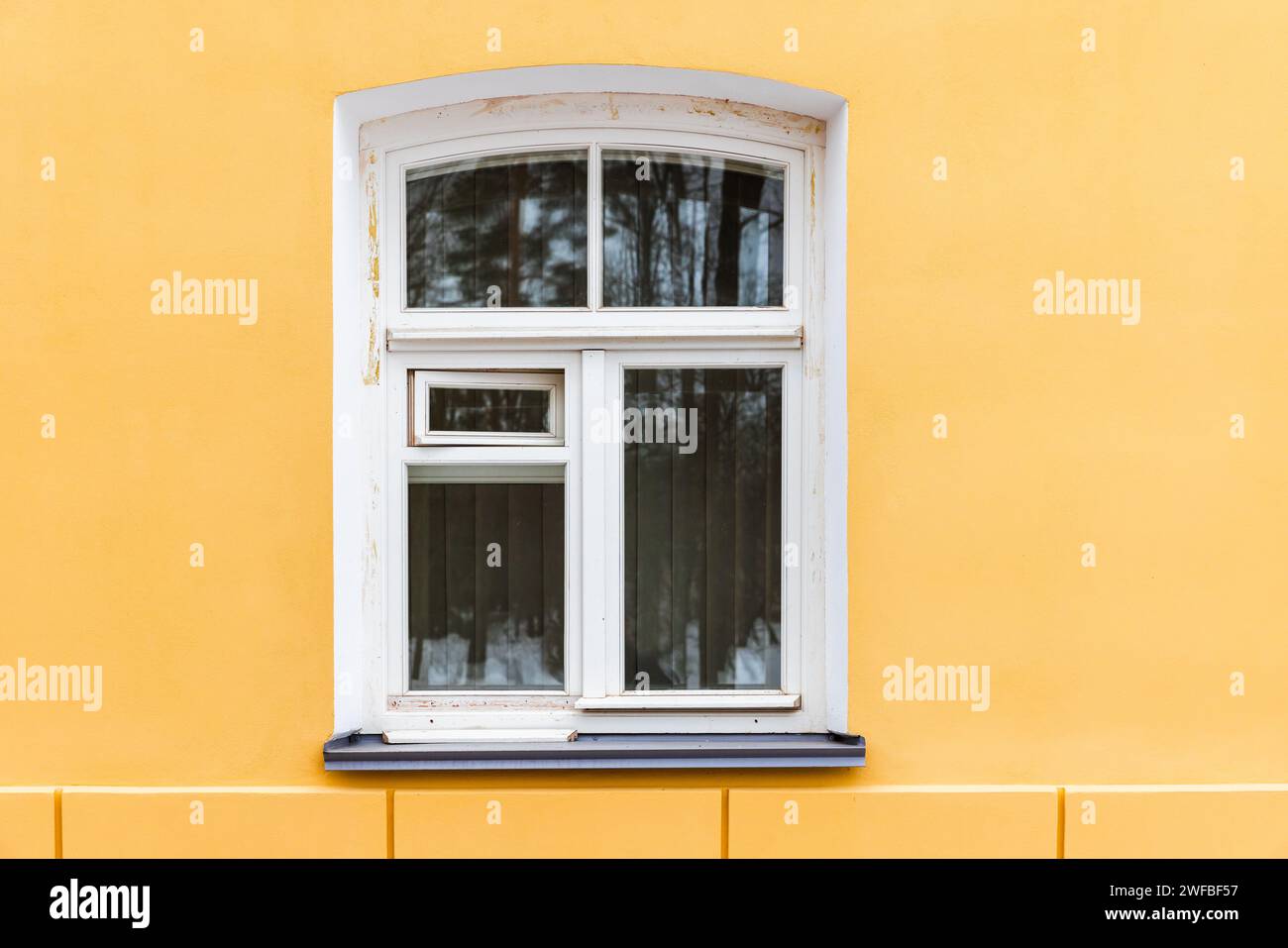 Bogenförmiges Fenster mit weißem Holzrahmen in gelber Wand, Hintergrundfotostruktur Stockfoto