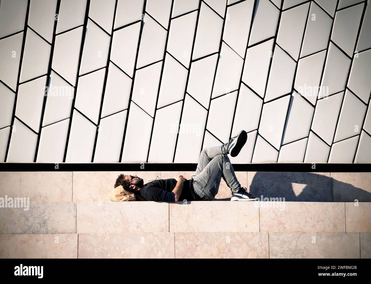 Ein junger Mann schlummert friedlich unter der Wärme der Sonne, umrahmt von den eleganten Linien einer modernen urbanen Kulisse Stockfoto