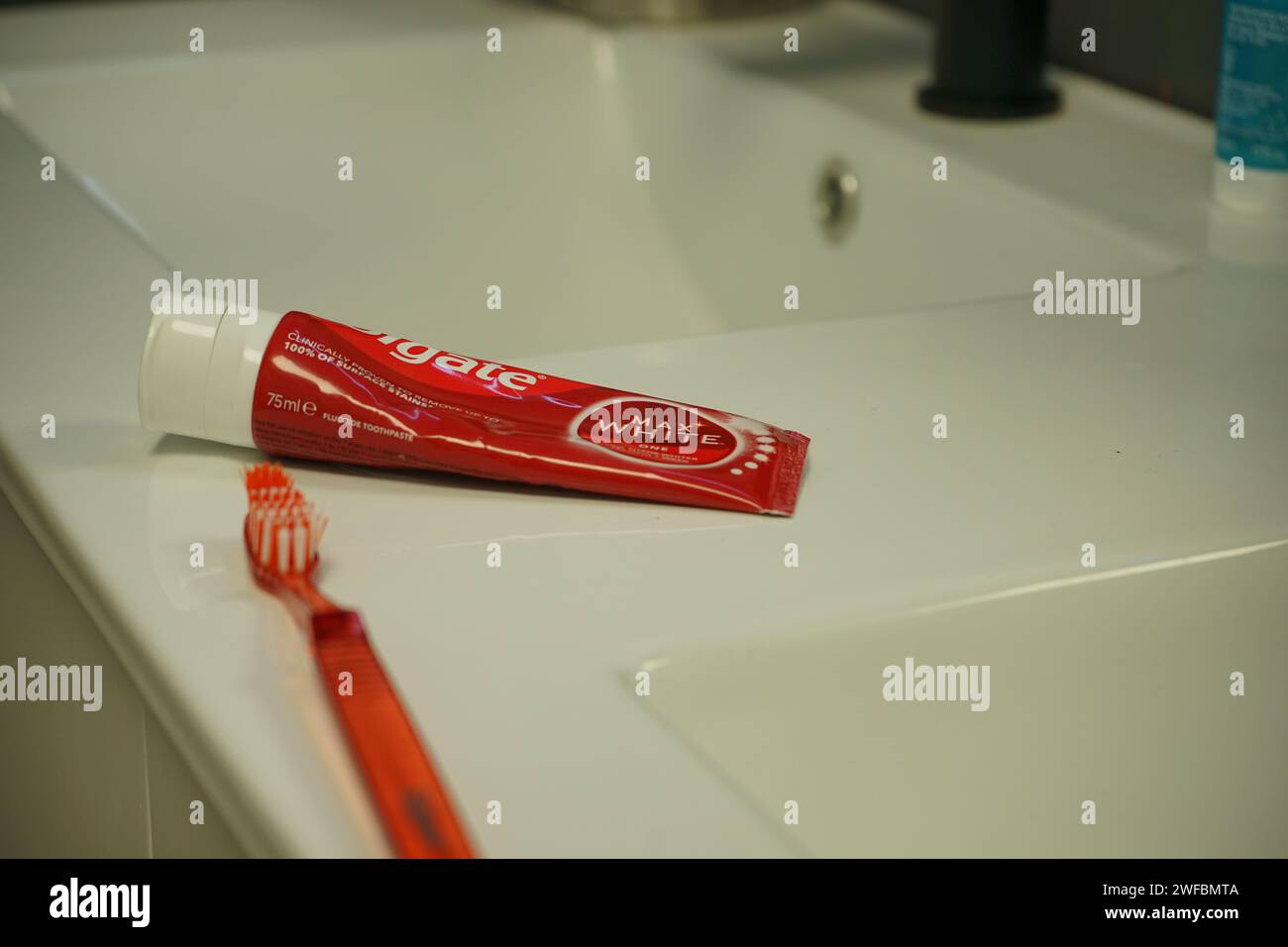 Red colgate Zahnpasta und Zahnbürste auf einer Badezimmertheke in der Nähe des weißen Waschbeckens Stockfoto