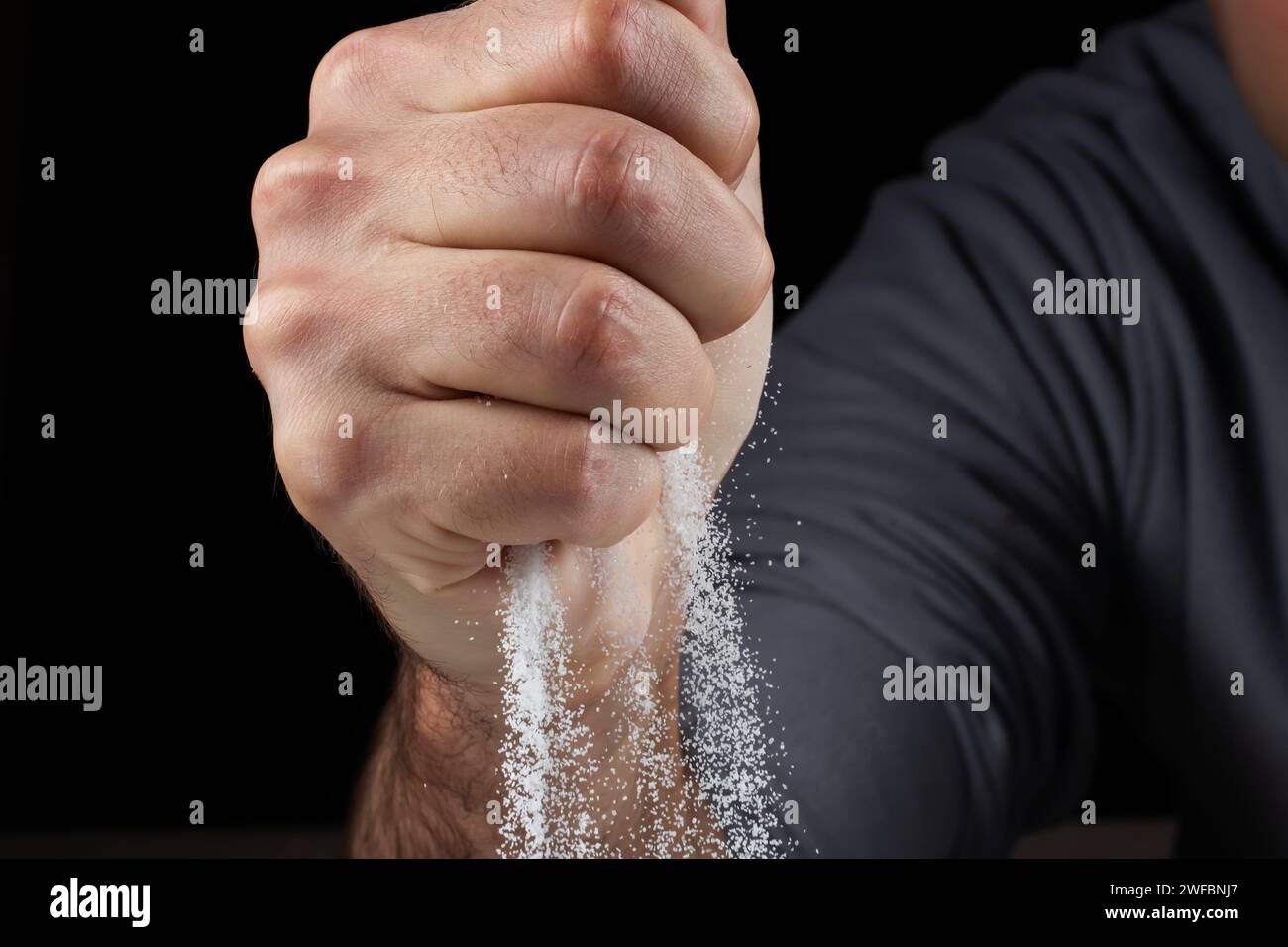 Ein Mann mit einer Handvoll weißen, trockenen Sand in ihren Händen, der Sand durch die Finger auf schwarzem Hintergrund verschüttet. Das Konzept des Lebensflusses. Nahaufnahme von pur-Körnern Stockfoto