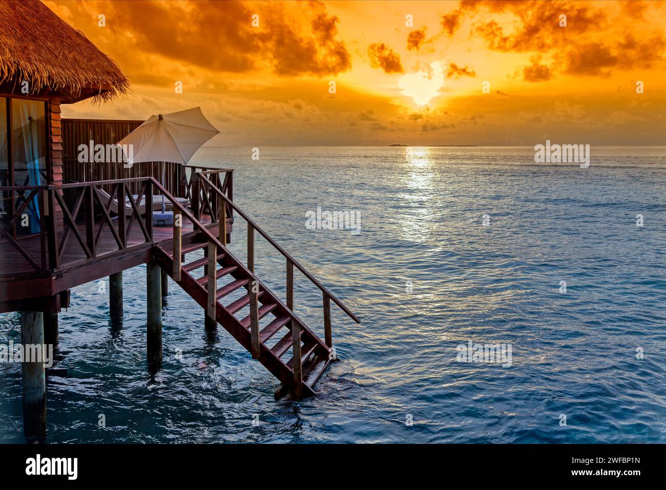 Sonnenaufgang oder Sonnenuntergang über Wasserbungalow auf Stelzen mit Treppen ins Meer auf einer tropischen Insel, Malediven, Indischen Ozean Stockfoto