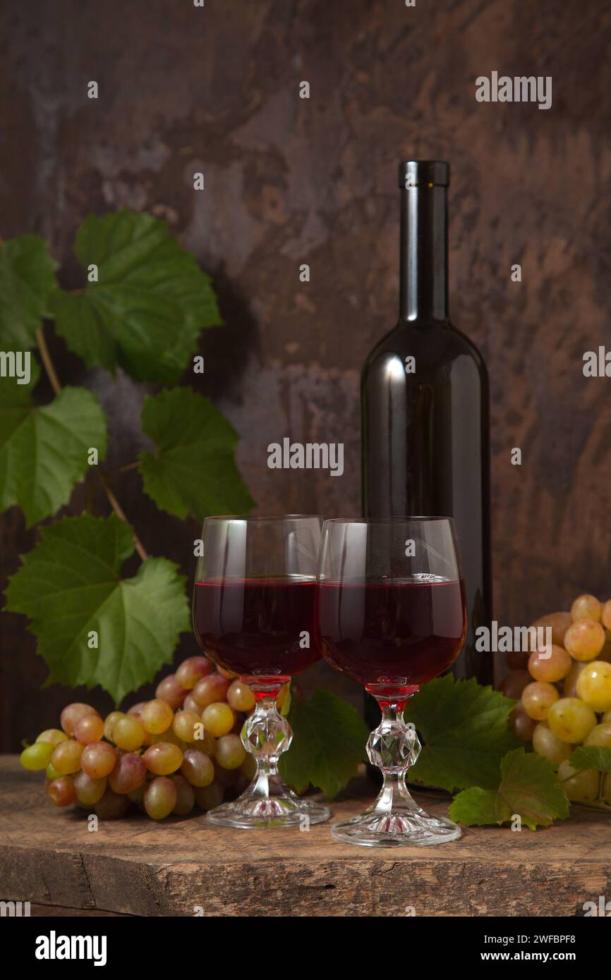 Das Konzept eines köstlichen alkoholischen Getränks, Wein und Trauben. Weinflasche, Gläser Rotwein und Trauben auf dunklem rustikalem Holzhintergrund mit Stockfoto