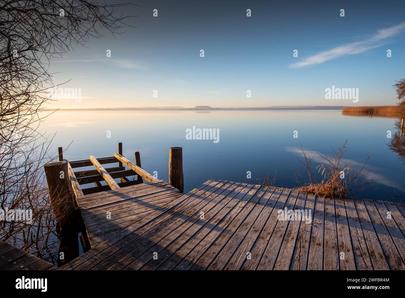 Fußgängerbrücke oder Steg bei Sonnenaufgang bei frostigem Wetter vor einem ruhigen, spiegelglatten See. Meditativer Blick über das Steinhuder Meer. Stockfoto