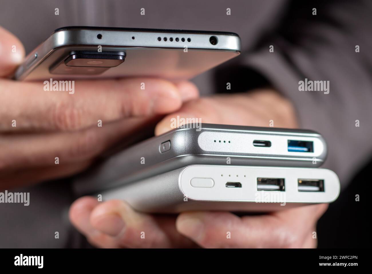 Der Mann hält Telefon und Ladegerät in der Hand. Powerbank und Smartphone in der Hand. Stromspargerät Powerbank Smartphone Stockfoto