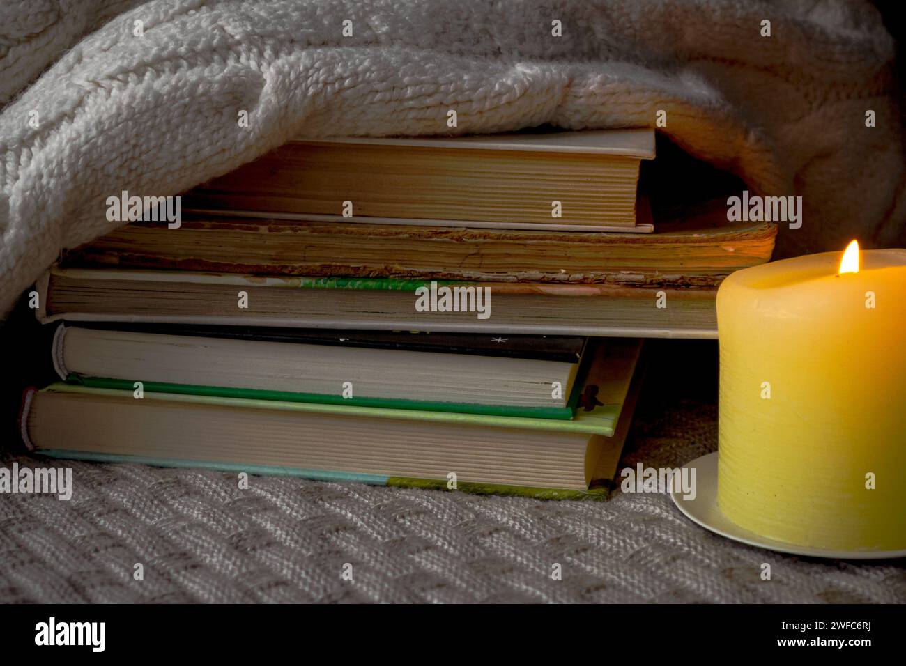 Ein Stapel Bücher und ein warmer Pullover auf einem gestrickten Karo bei Kerzenschein Stockfoto