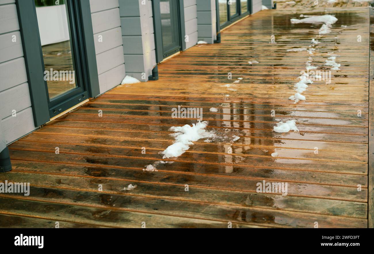 Schmelzendes Eis und Schnee auf dem Hartholzboden der Terrasse, Stockfoto