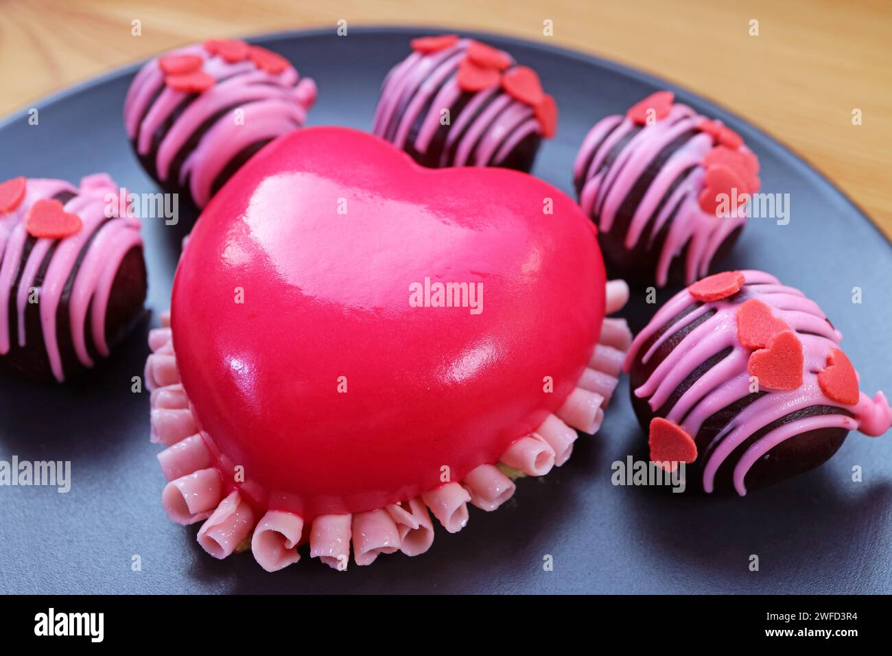 Großaufnahme des herzförmigen Erdbeermousse-Tortes in leuchtendem Pink mit Schokoladenkuchen auf schwarzer Platte Stockfoto