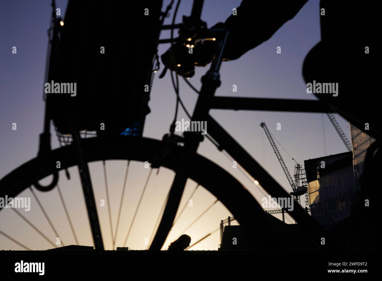 Die Silhouette eines Radfahrers, der mit einer Frau vorbeigeht, die durch die Speichen des Rades in der frühen Morgensonne des Winters gesehen wird. Stockfoto