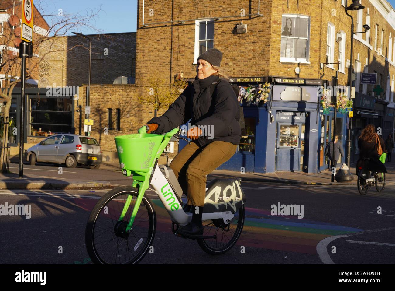 Eine weiße Fahrradfahrerin pendelt in Hackney, East London, in der frühen Morgensonne, mit einem Lime Bike. Stockfoto