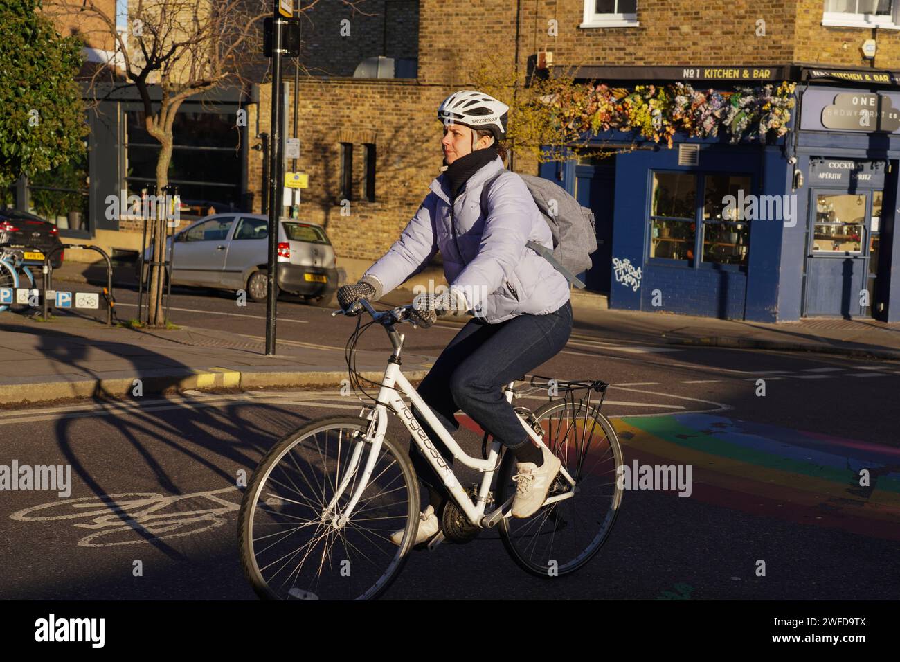 Eine weiße Fahrradfahrerin pendelt in Hackney, East London, in der frühen Wintersonne auf einem weißen Fahrrad, mit einem weißen Helm. Stockfoto