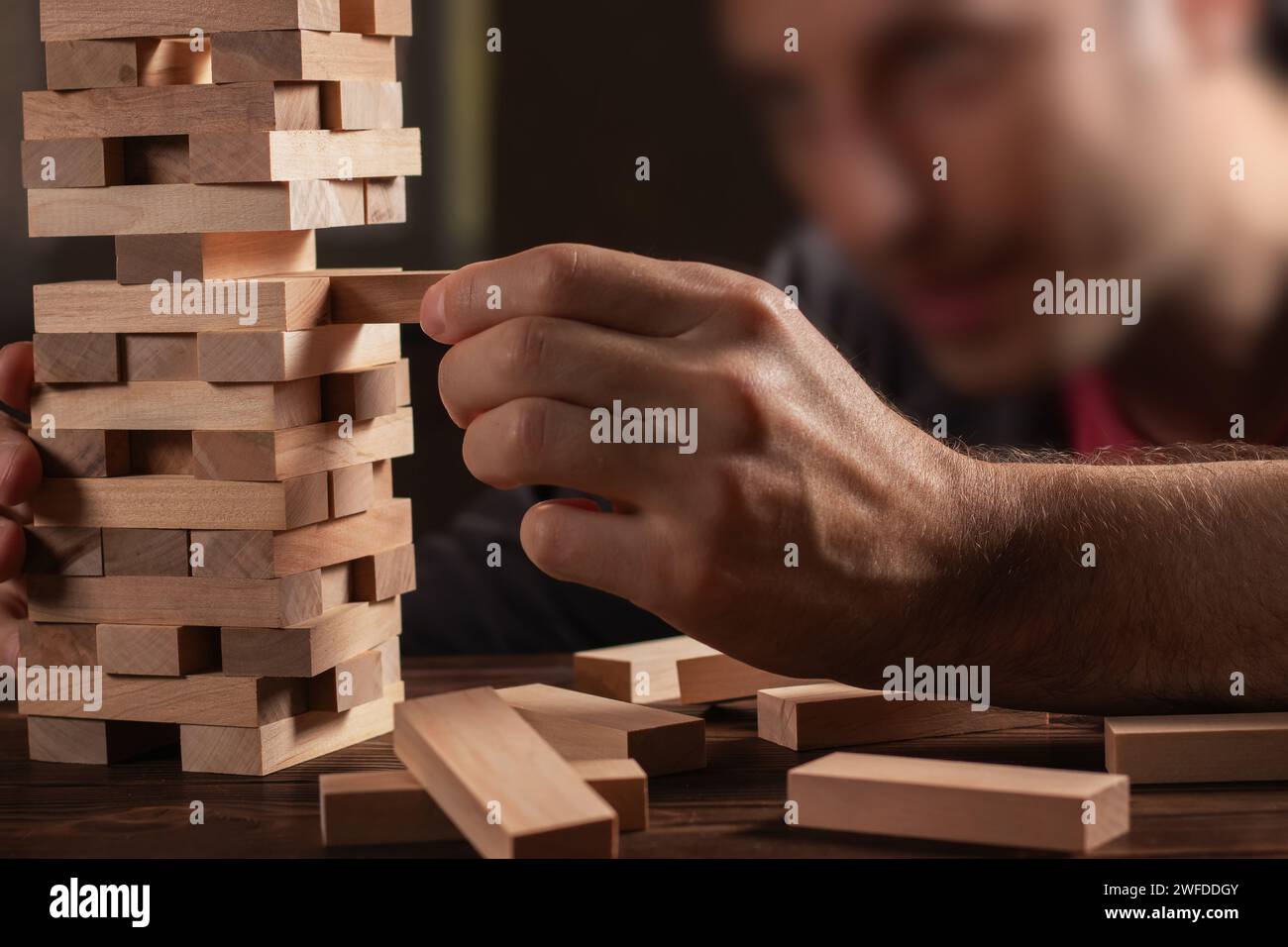 Man händet einen Stapel Holzblöcke für das Spiel auf einem dunkelbraunen Tisch, während man während der Quarantäne zu Hause bleibt, Familienaktivitäten zu Hause, Partybrett offline Stockfoto