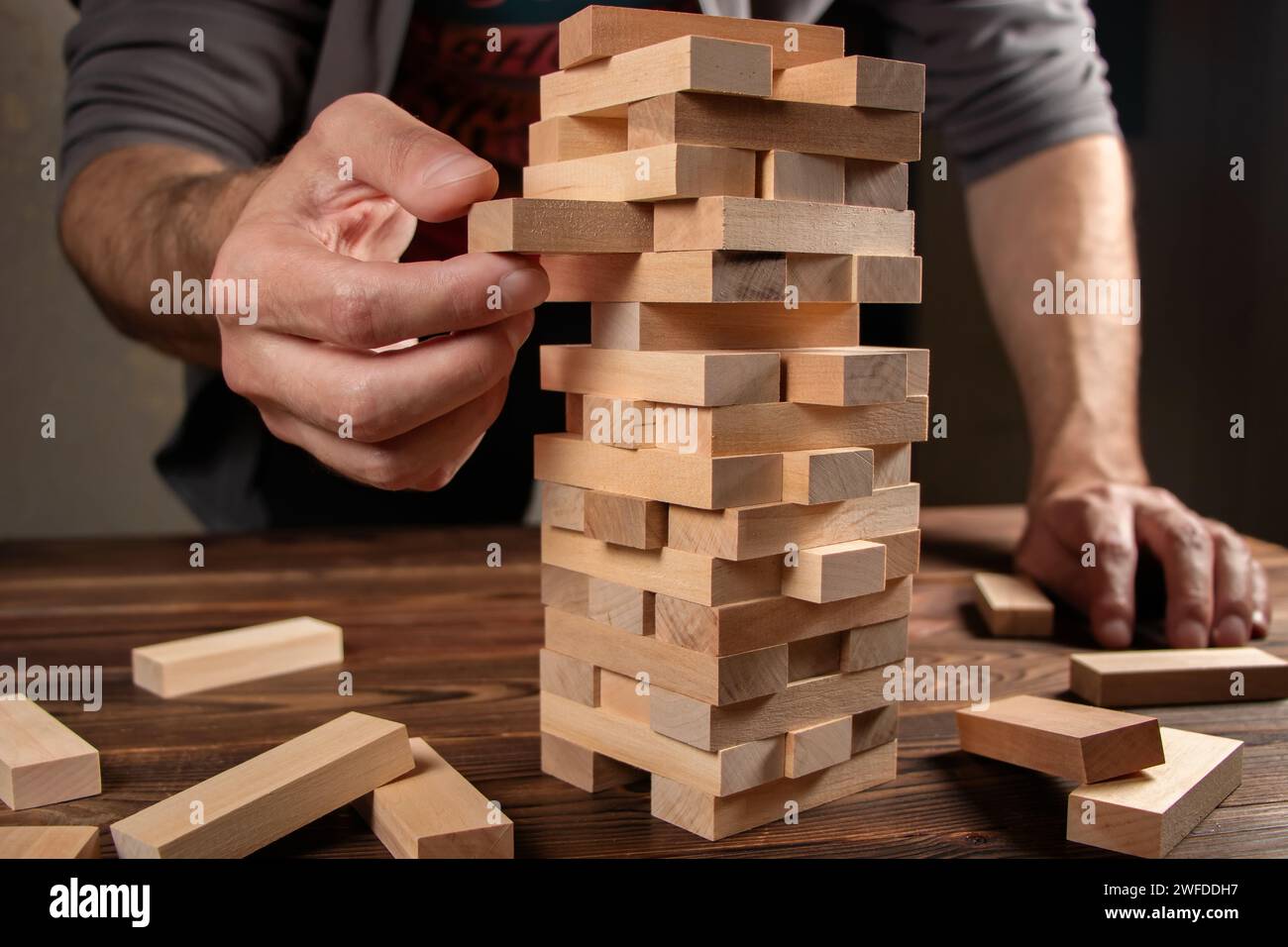 Hand des Ingenieurs spielt ein Blockholz Turm Spiel Jenga auf Blueprint oder Architekturprojekt. Stockfoto