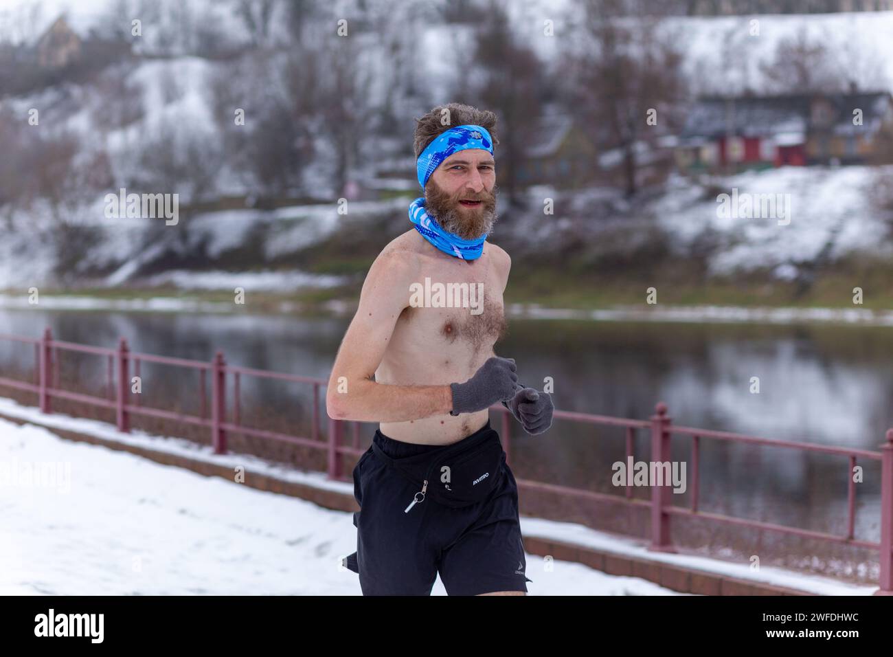 Grodno, Weißrussland - 28. Januar 2024: Ein Mann mit nacktem Oberkörper läuft während des traditionellen jährlichen Temper-fest-Rennens an einem schneebedeckten Damm entlang Stockfoto