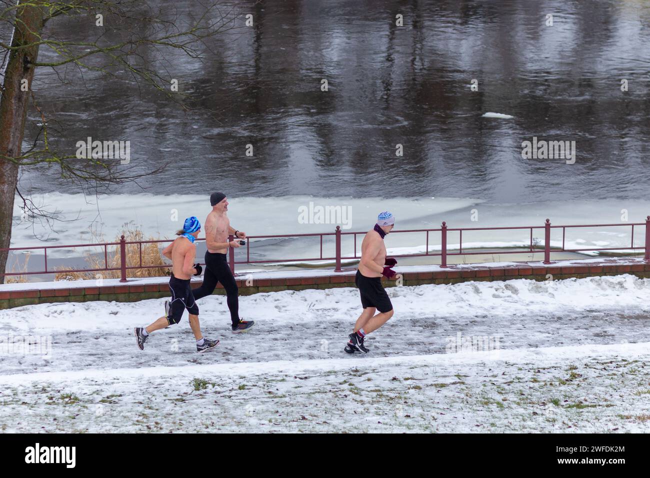 Grodno, Weißrussland - 28. Januar 2024: Drei Mans mit nacktem Oberkörper entlang eines schneebedeckten Damms während des traditionellen jährlichen Temper-fest-Rennens Stockfoto
