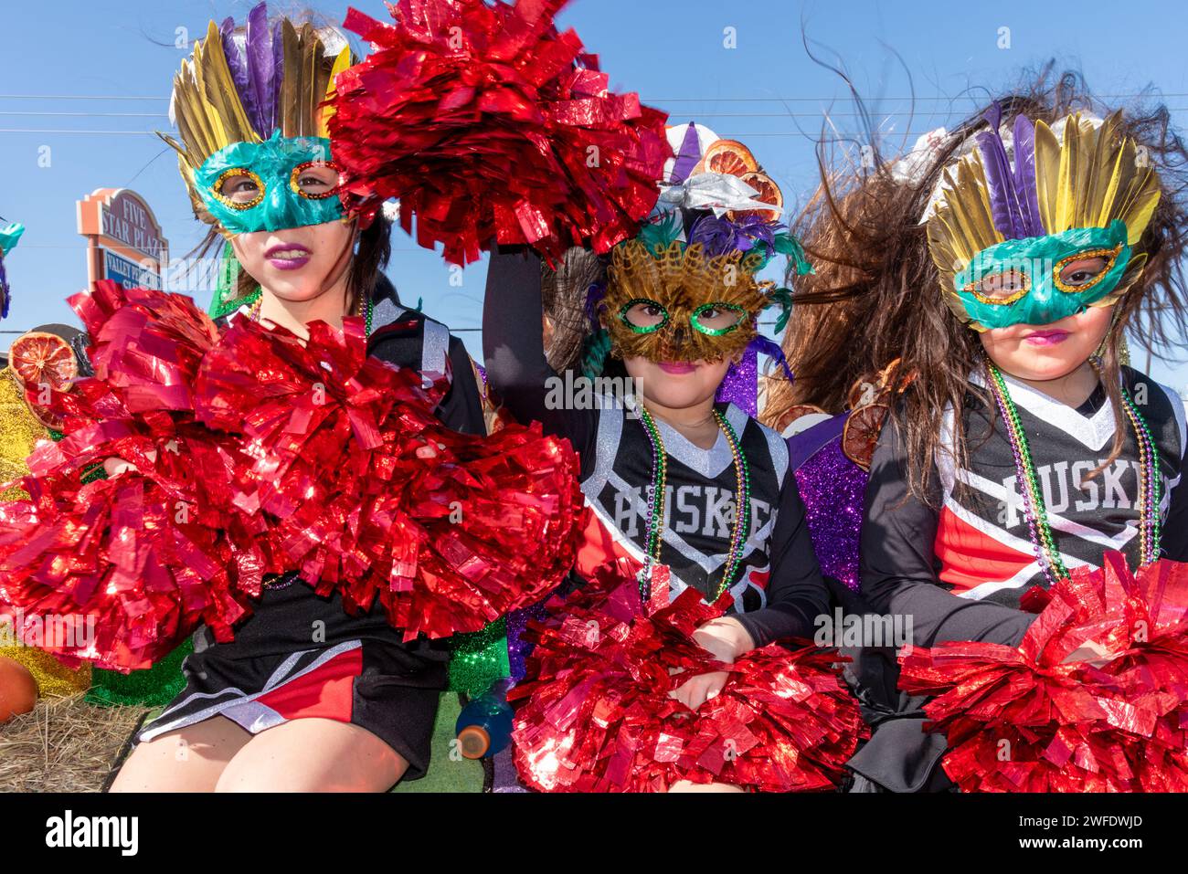 Drei junge Mädchen in Kostümen und Masken, die Pompons in der 92. Jährlichen Texas Citrus Fiesta Parade of Orangen, Mission, Texas, USA, halten. Stockfoto