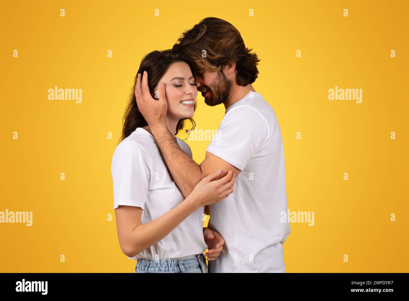 Intime Paare in weißen T-Shirts teilen einen zärtlichen Moment, während der Mann sanft das Gesicht der Frau wiegt Stockfoto