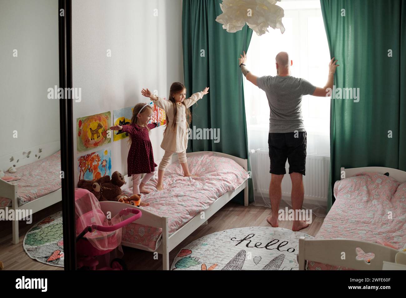 Rückansicht eines jungen Glatzen-Mannes in Haushaltswaren, der morgens grüne Vorhänge auföffnete, während er neben seinen zwei Töchtern beim Sport stand Stockfoto