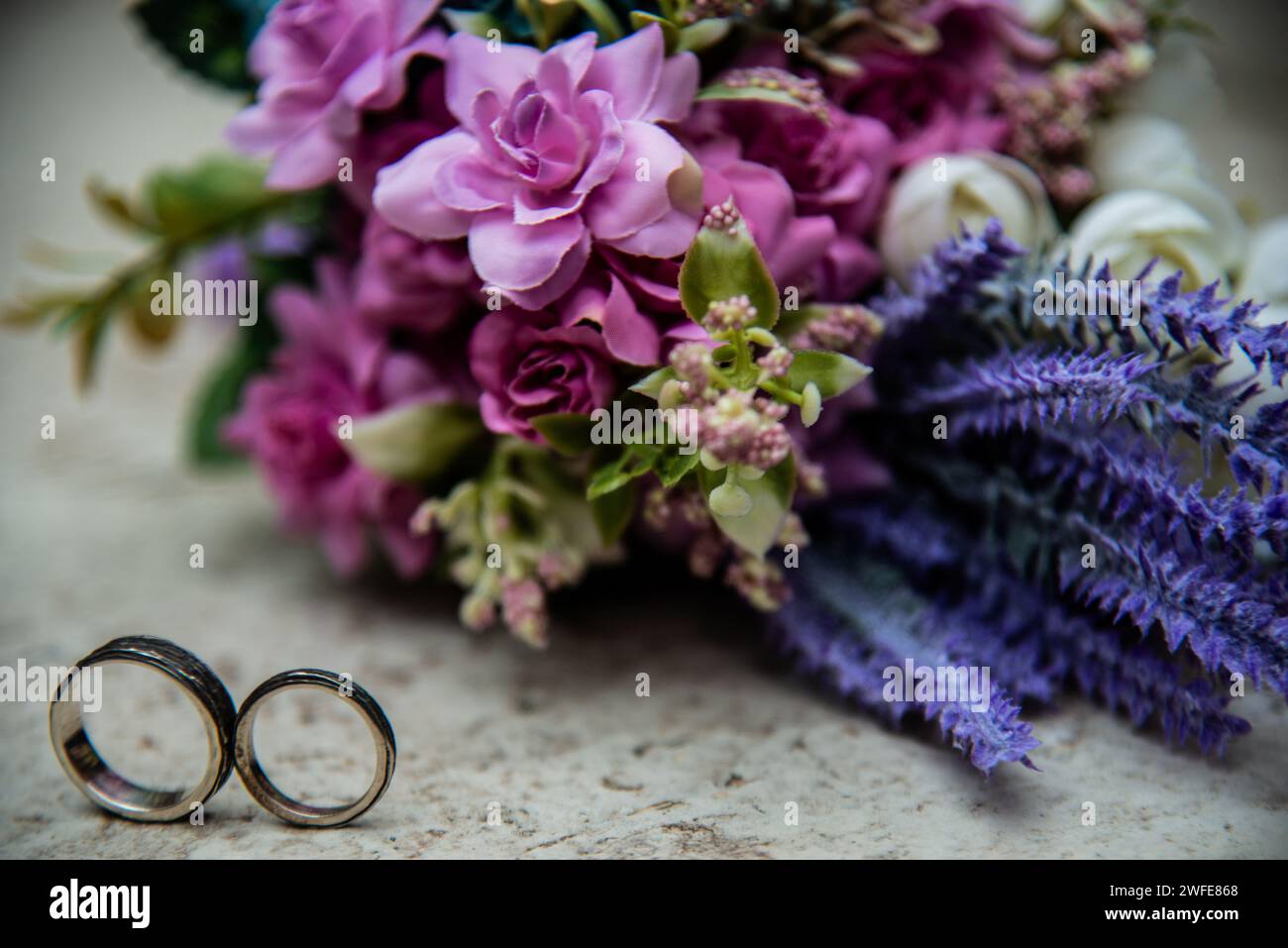 Zwei Eheringe und ein Blumenstrauß auf dem Boden für unvergessliche Hochzeitsfotos Stockfoto
