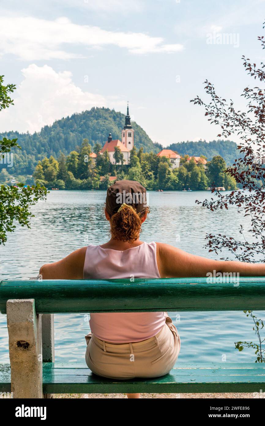 Frau, die auf einer Bank sitzt, mit dem Rücken gewendet und über den Bleder See in Slowenien blickt. Stockfoto