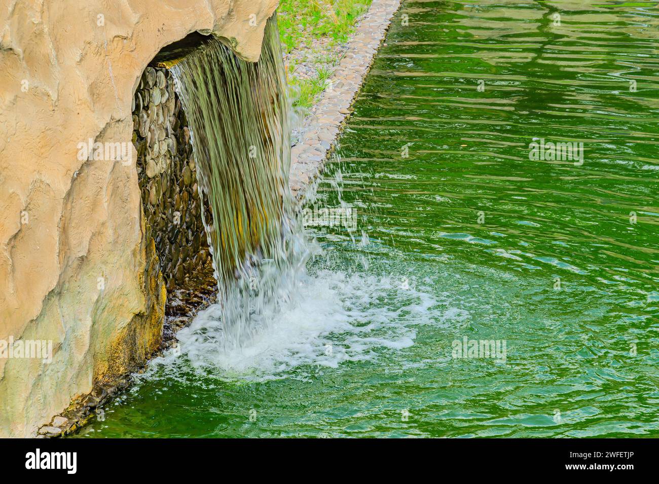 Ein kleiner dekorativer Wasserfall im Garten. Landschaftsdesign. Kleiner künstlicher Wasserfall in einem künstlichen tropischen Garten Stockfoto