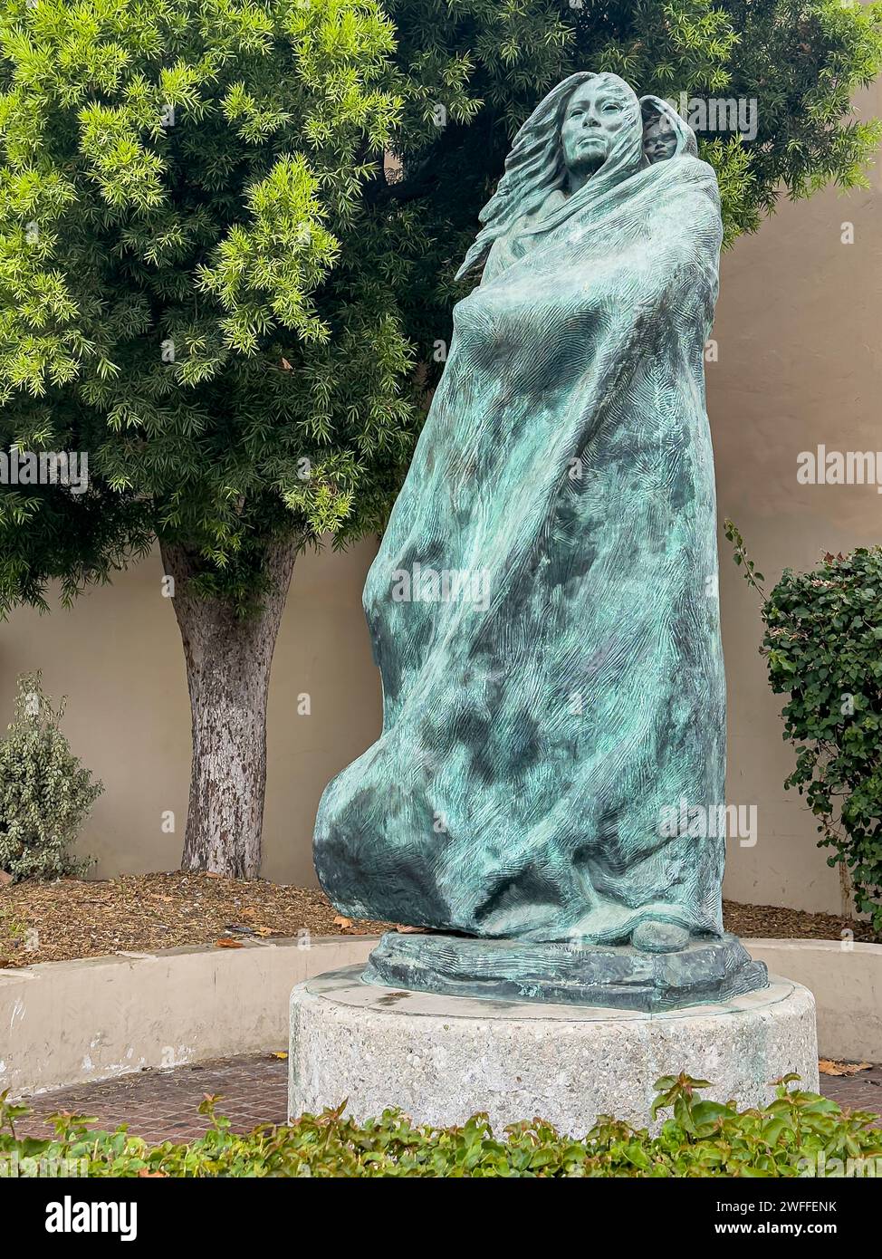Santa Barbara, CA, USA - 19. Januar 2024: Grüne Bronzestatue von Juana Maria und Kind. Grünes Laub hinten. Einsame Frau von San Nicolas Isla Stockfoto