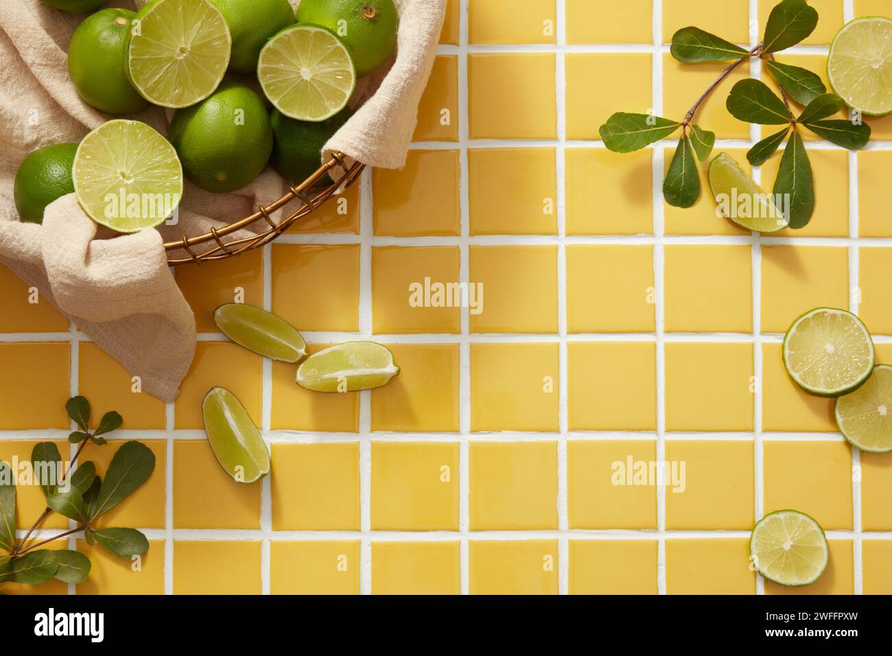 Ein Bambuskorb mit Limette, angeordnet mit Baumzweig und Limettenscheiben auf gelbem Hintergrund. Leerer Raum, um Schönheitsprodukte zu zeigen, die aus Li extrahiert wurden Stockfoto