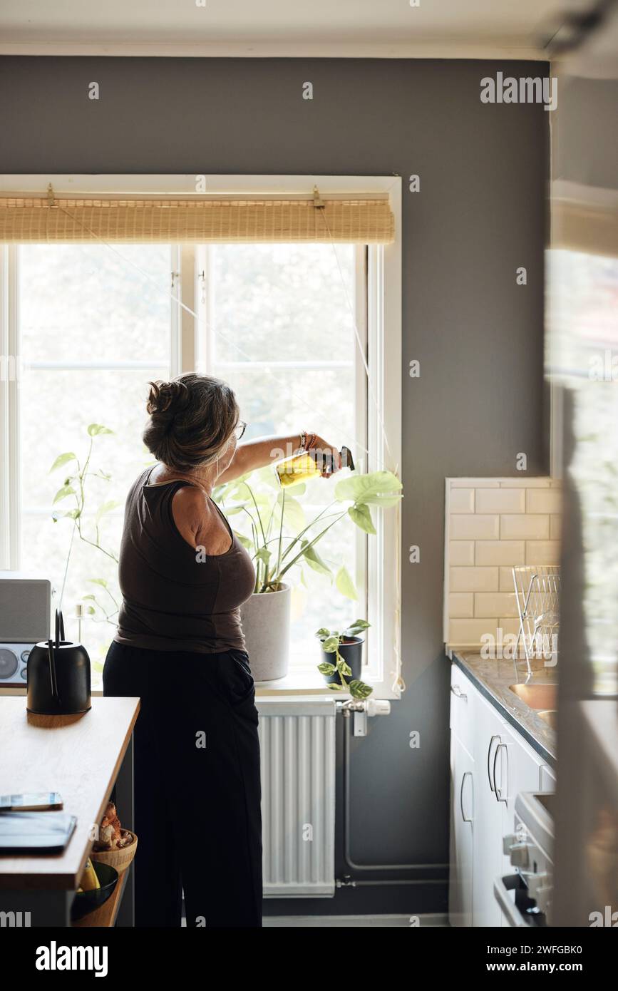 Frau mit Behinderung sprüht Wasser auf Pflanzen zu Hause Stockfoto