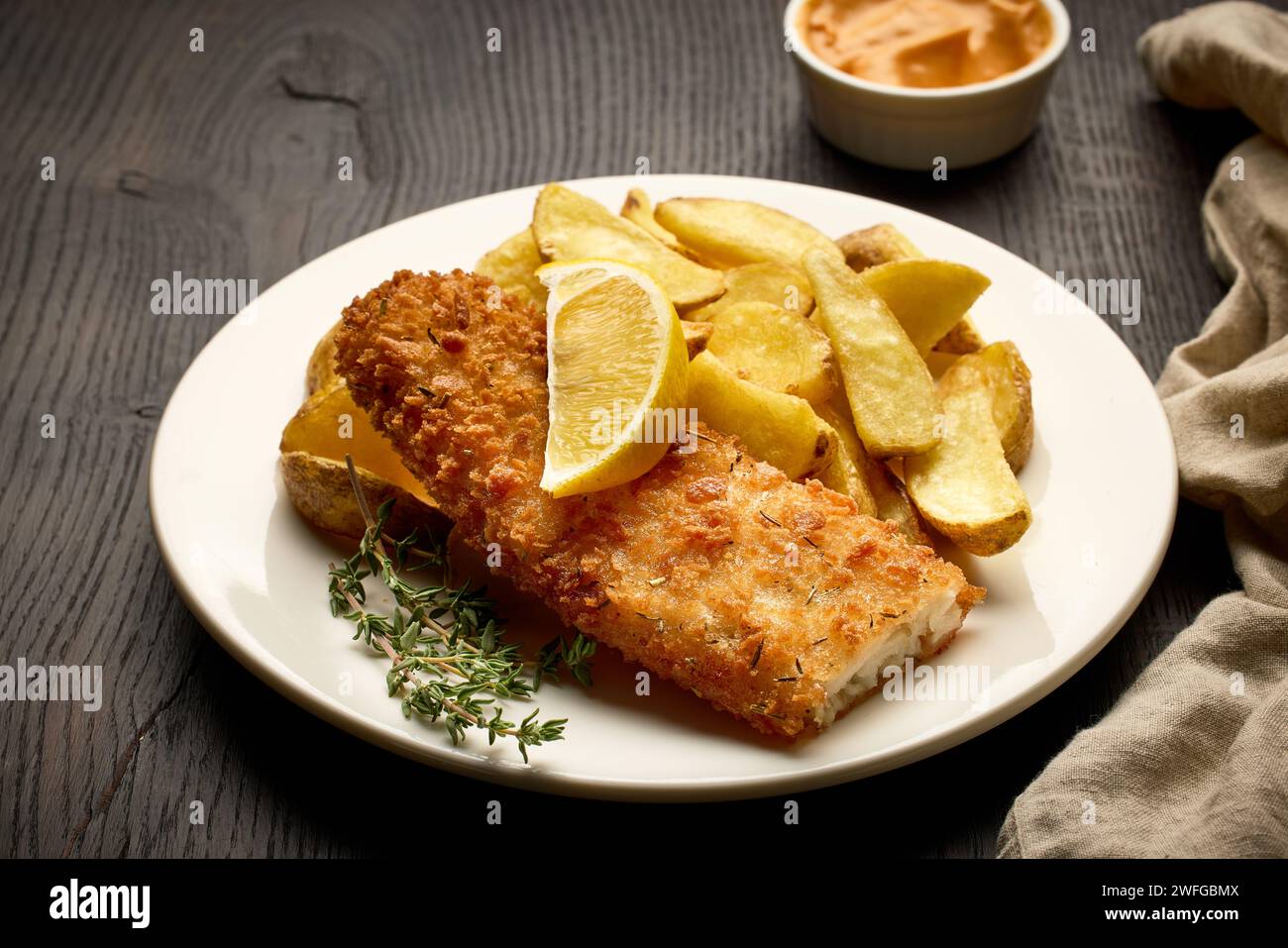 Teller mit Fish and Chips, paniertem Fischfilet und gebratenen Kartoffelscheiben auf dunklem Holztisch Stockfoto