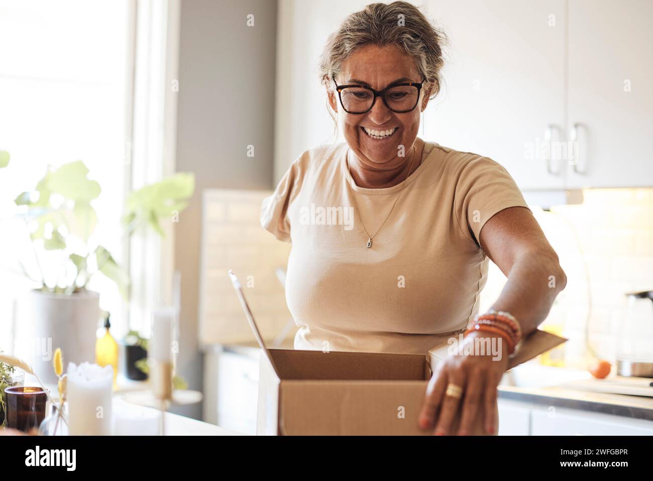 Glückliche Frau mit Behinderung, die Überraschungspaket in der Küche zu Hause eröffnet Stockfoto