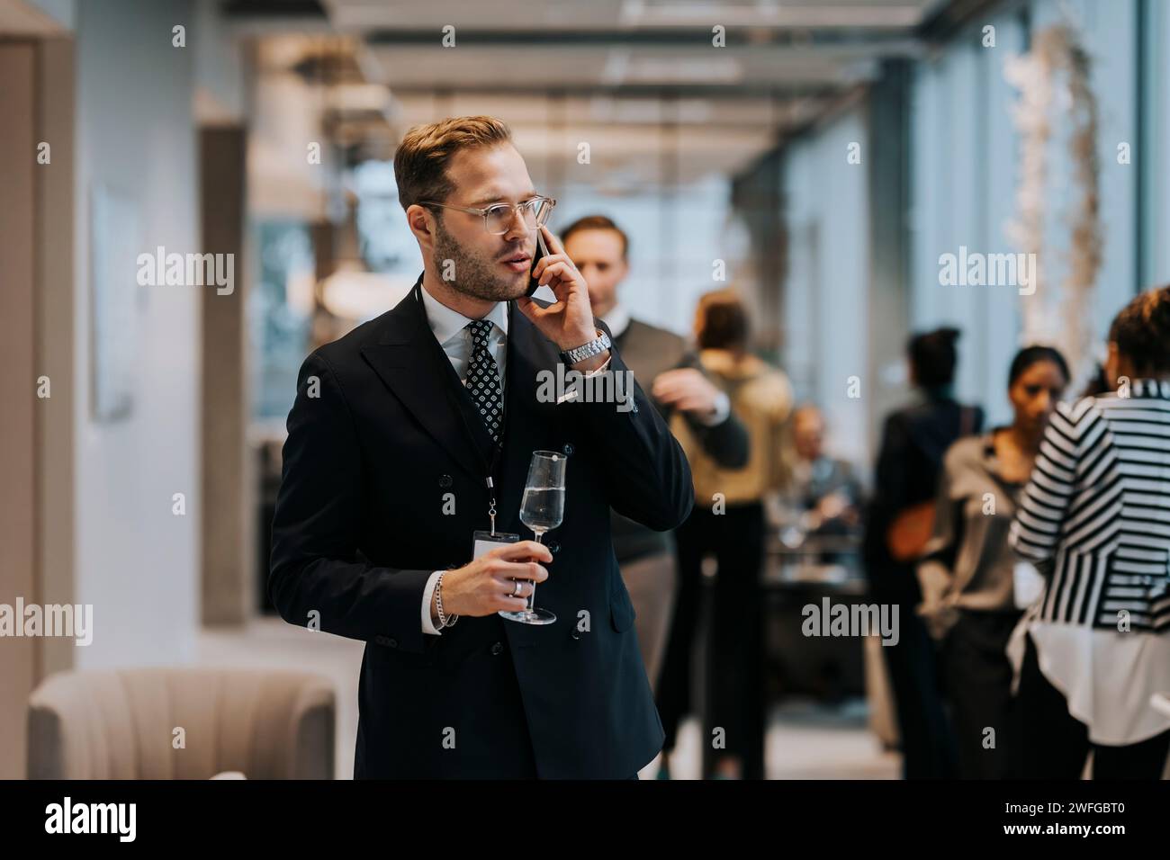 Junger Geschäftsmann mit Sektflöte, während er während einer Geschäftskonferenz auf dem Handy spricht Stockfoto