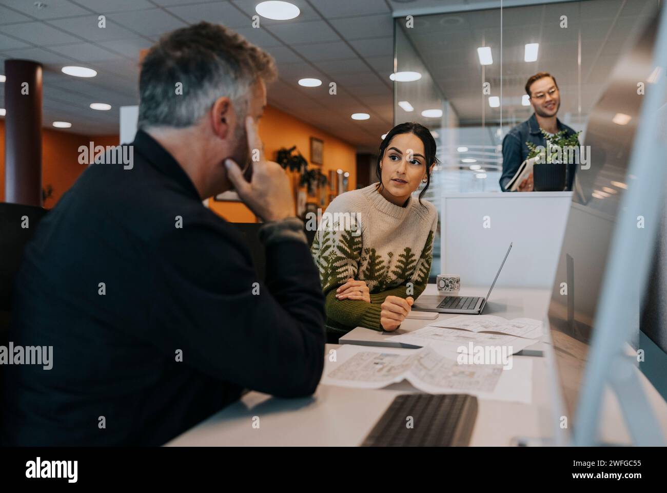 Geschäftsfrau diskutiert mit reifem Geschäftsmann, der am Schreibtisch im Büro sitzt Stockfoto