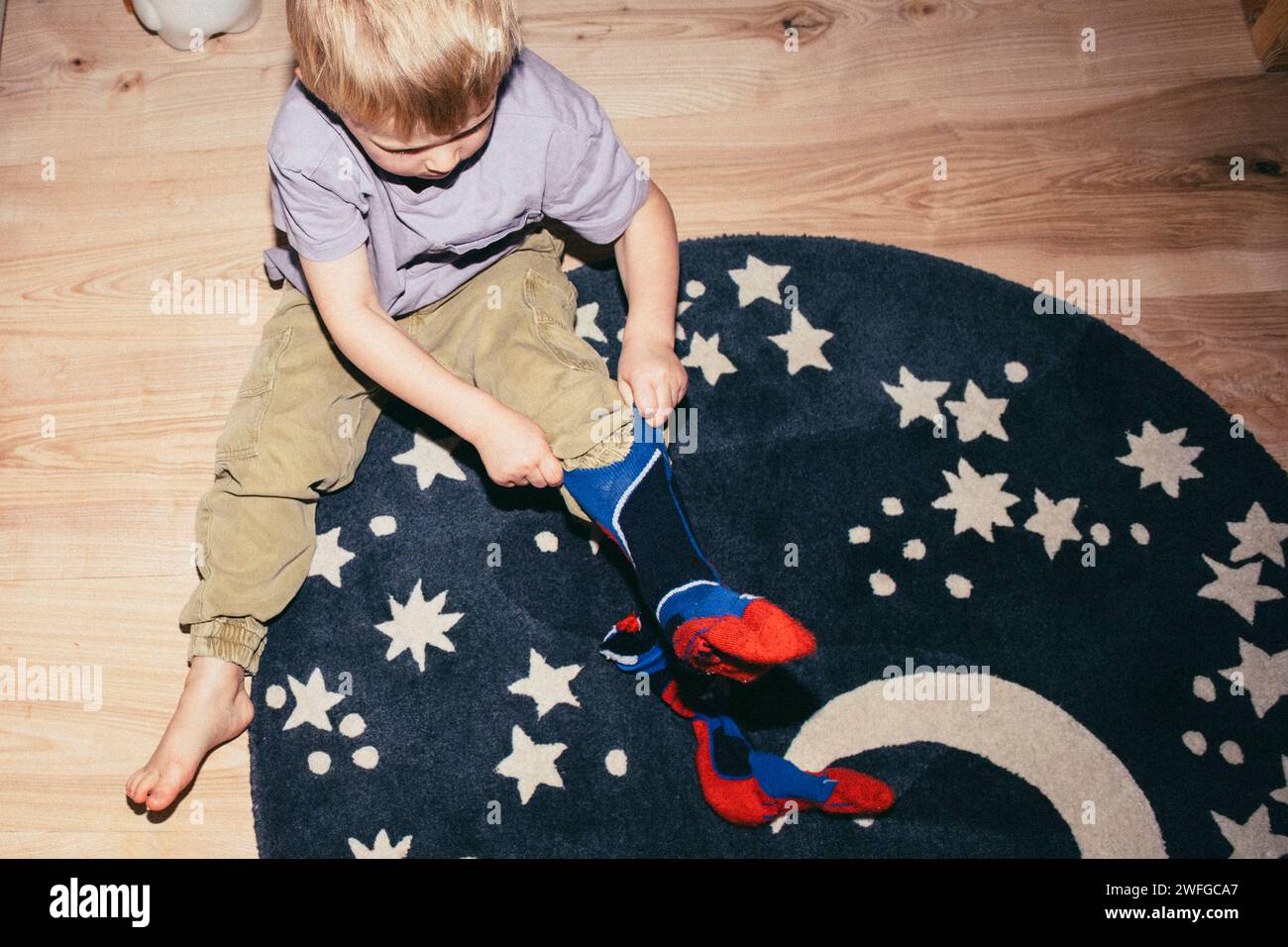 Hochwinkelansicht eines Jungen, der Socken trägt, während er zu Hause auf dem Teppich sitzt Stockfoto