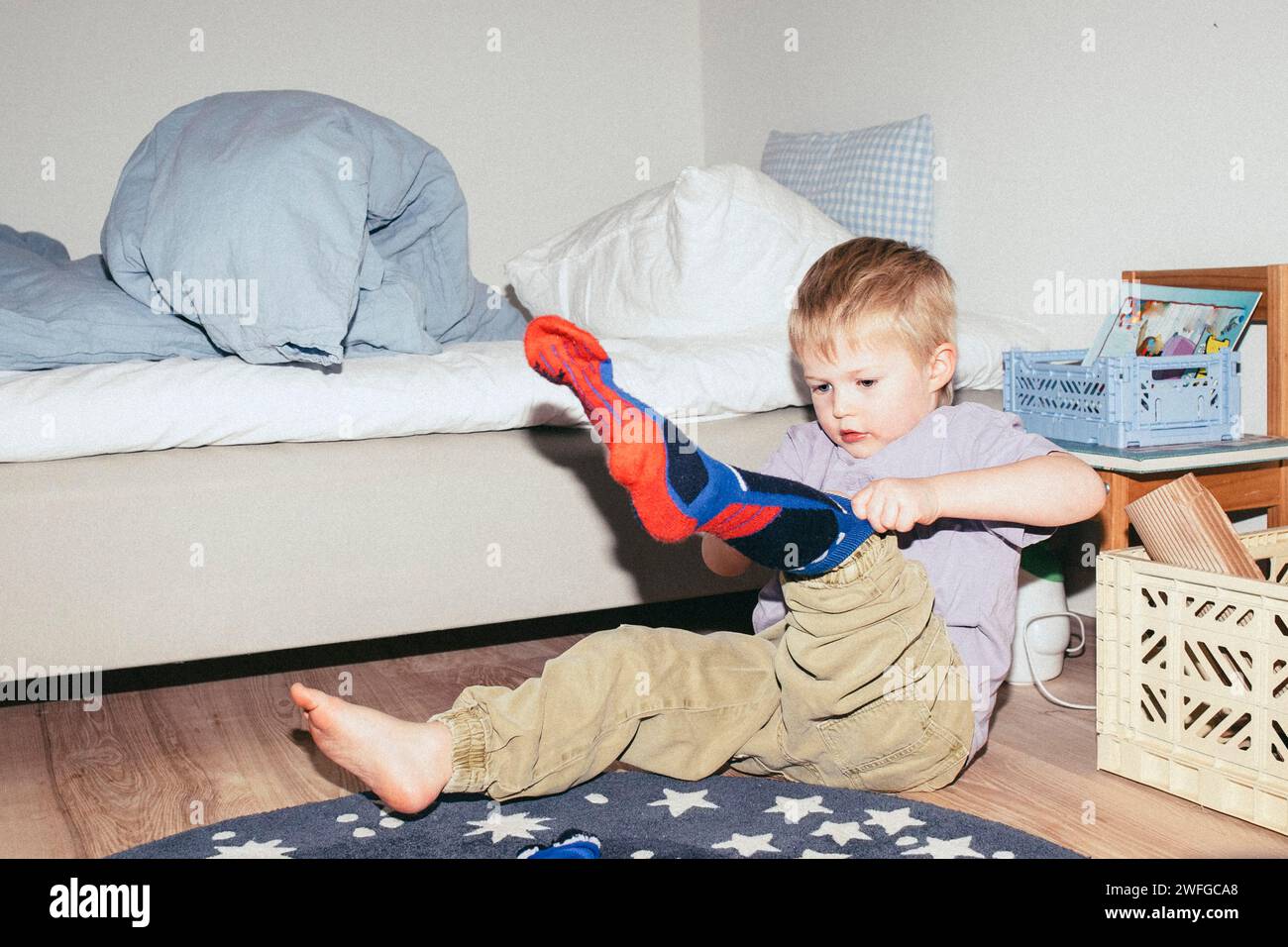 Junge, der Socken trägt, während er zu Hause auf dem Boden neben dem Bett sitzt Stockfoto