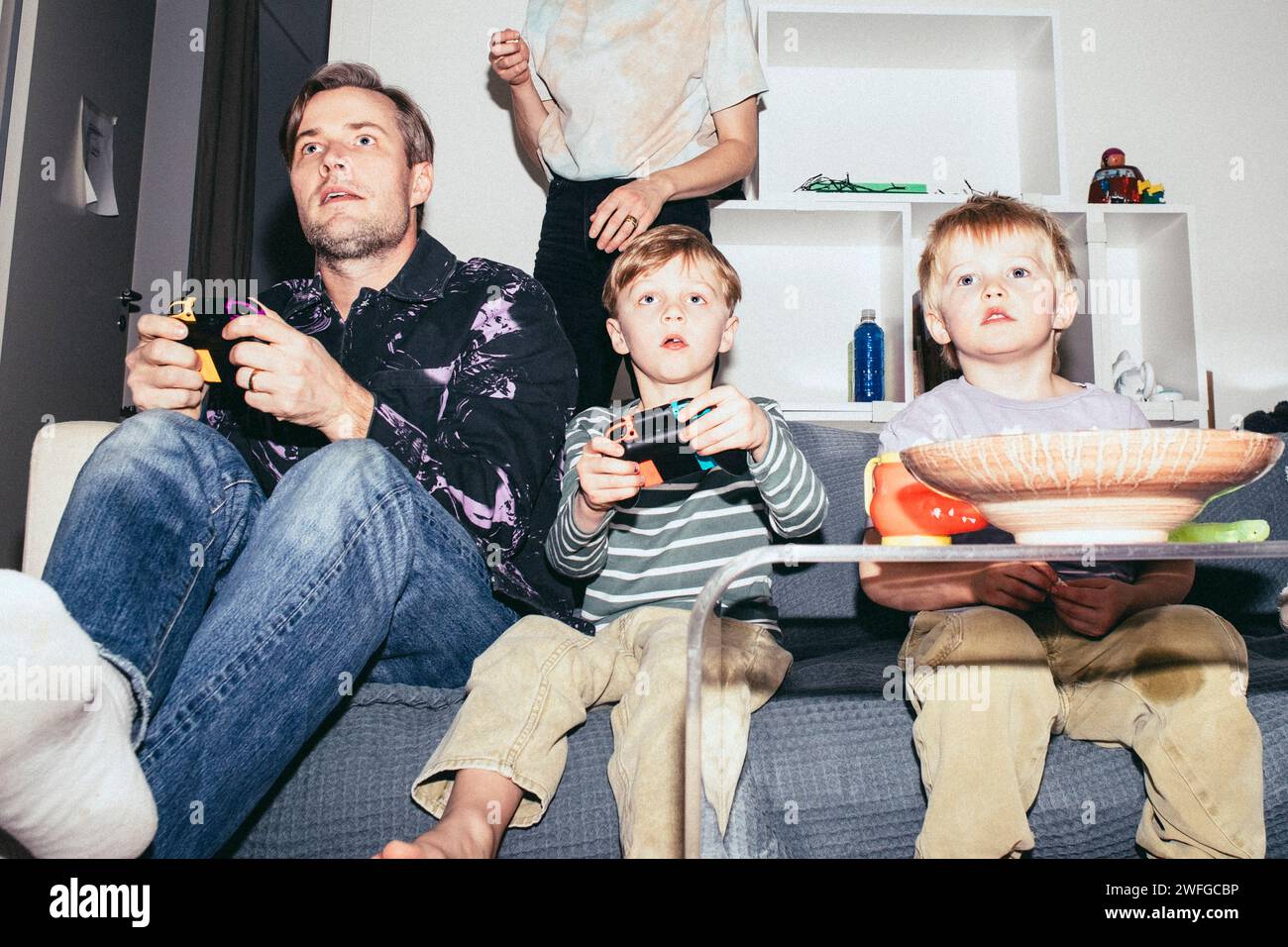 Vater spielt Videospiel mit Sohn, während er zu Hause auf dem Sofa sitzt Stockfoto