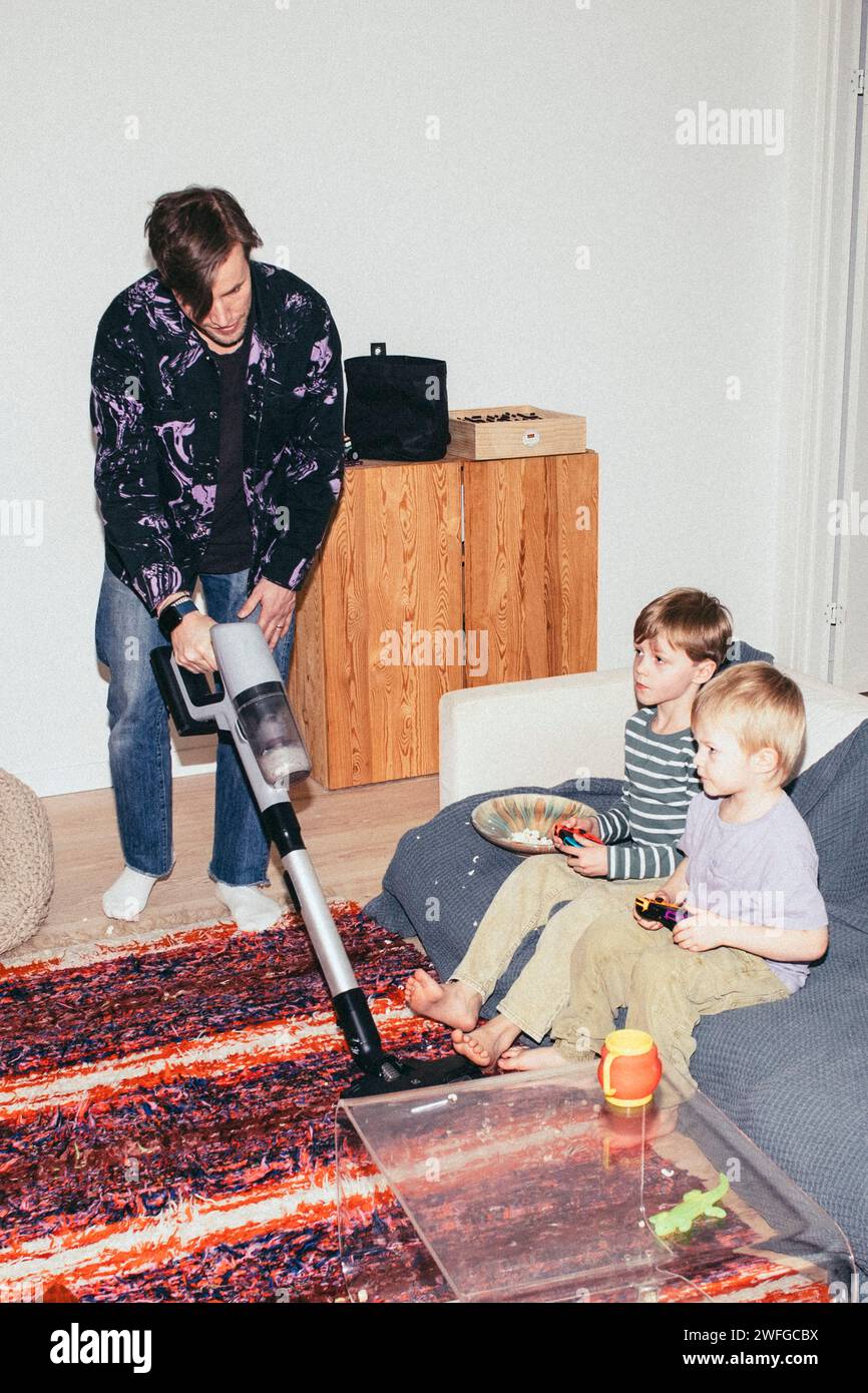 Vater saugt Boden, während Söhne zu Hause Videospiele spielen Stockfoto