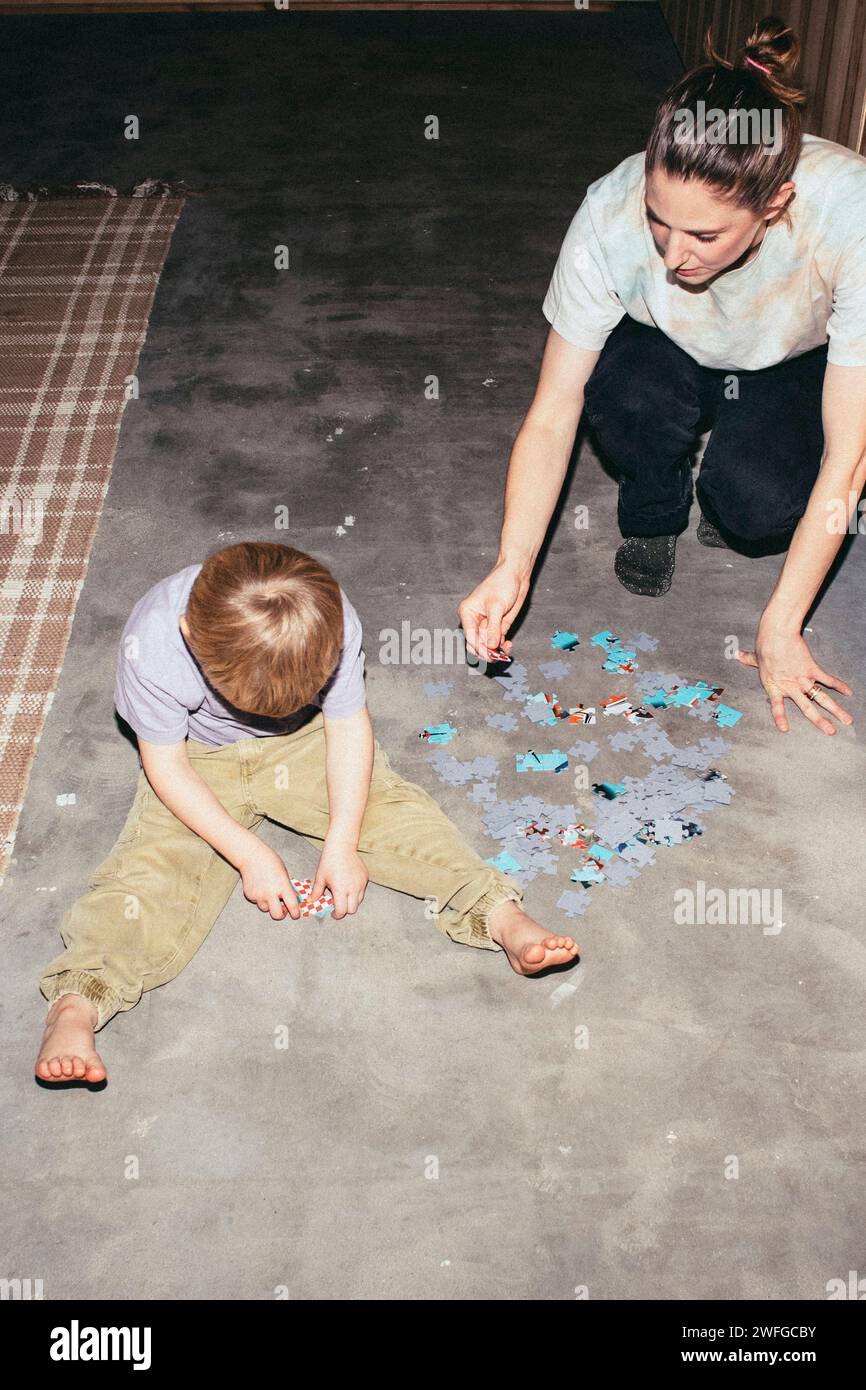 Hochwinkelansicht eines Jungen, der mit seiner Mutter Rätsel löst, während er zu Hause auf dem Boden sitzt Stockfoto