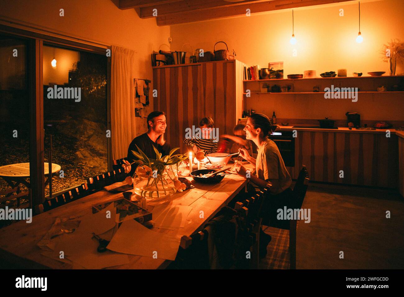 Glückliche Familie, die Kerzenabendessen genießt, während sie zu Hause am Esstisch sitzt Stockfoto