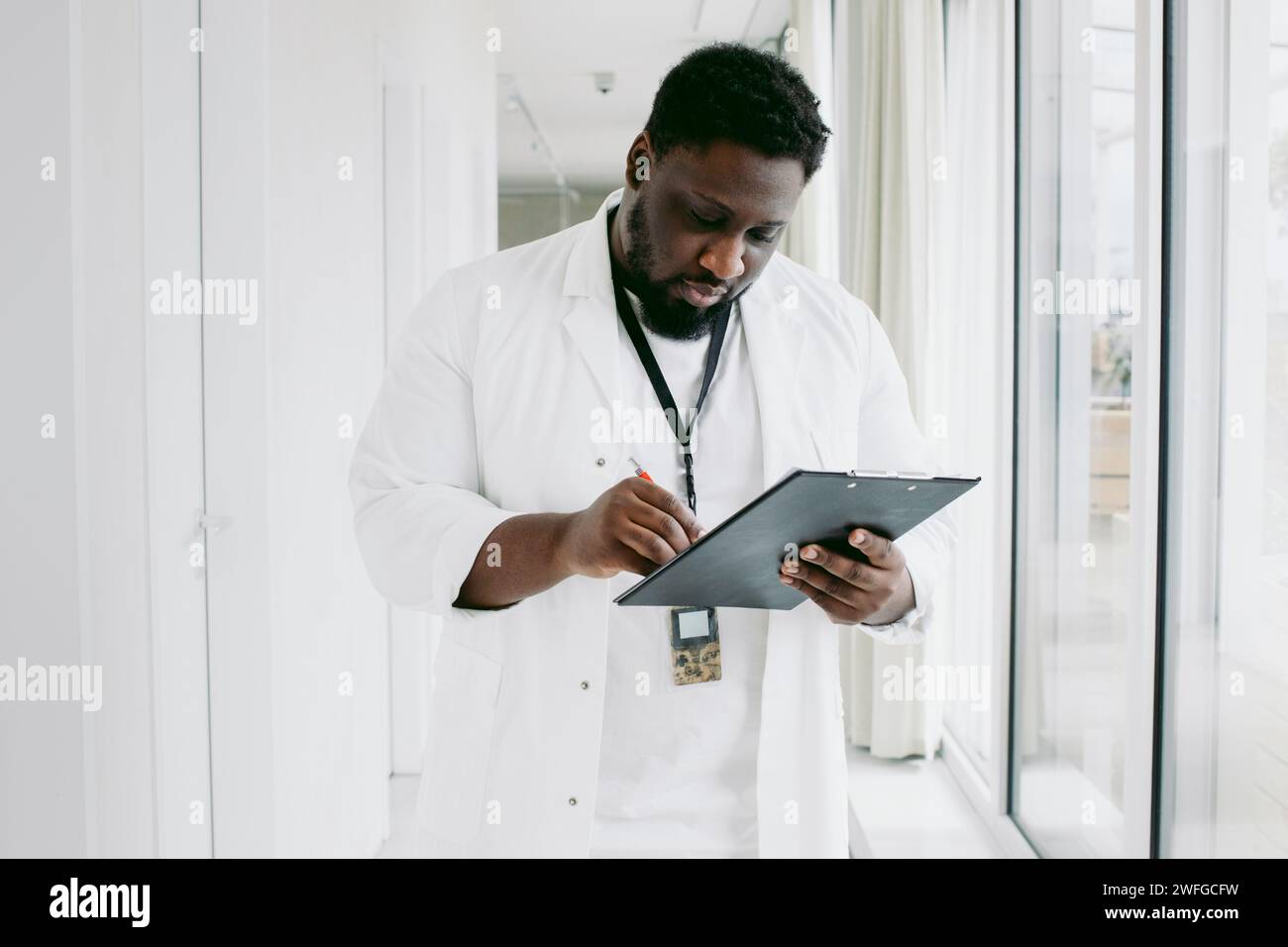 Junge Ärztin, die im Krankenhauskorridor auf das Klemmbrett schreibt Stockfoto