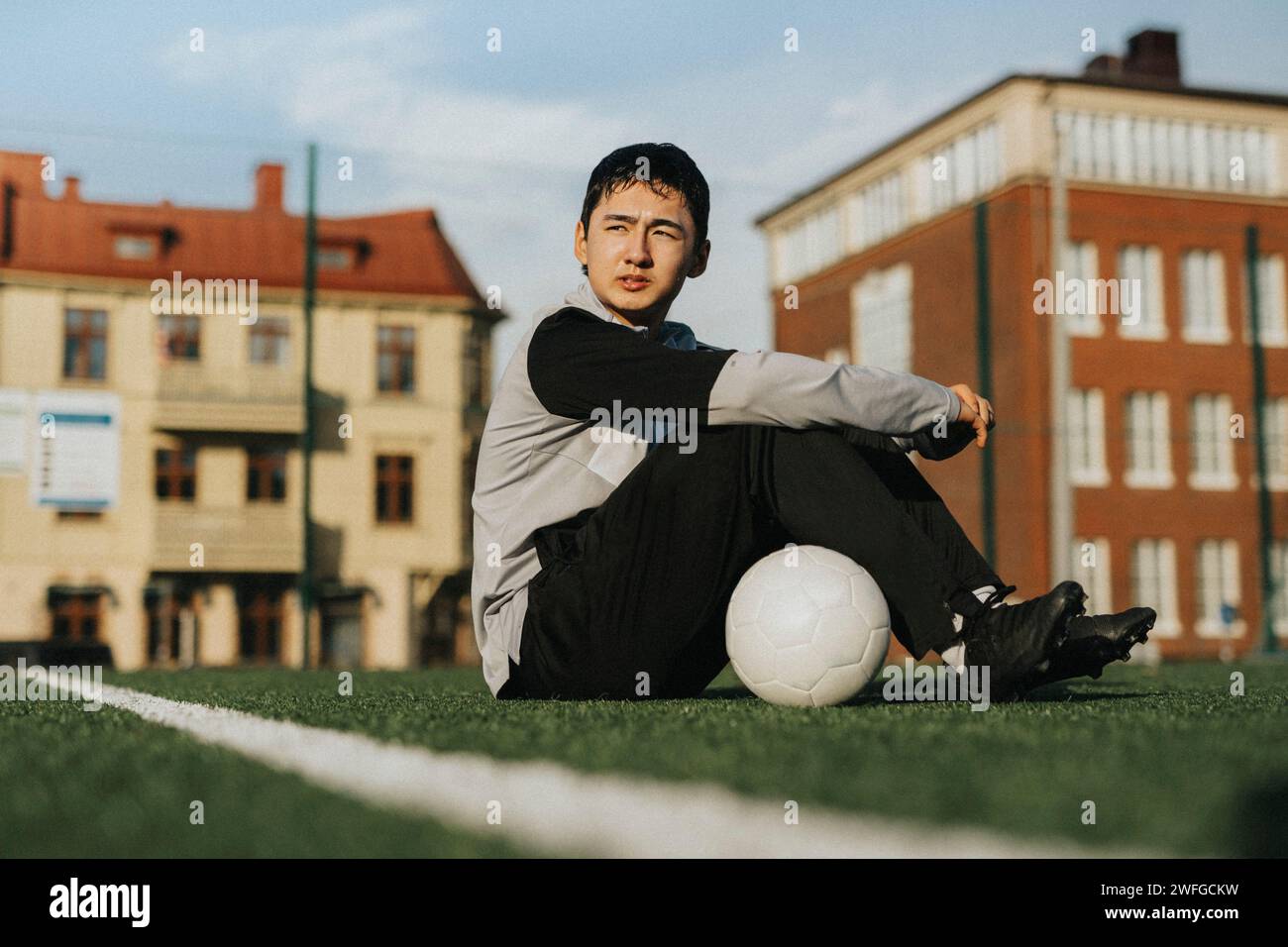 Ehrgeiziger Teenager mit Fußball, der auf dem Sportplatz sitzt Stockfoto