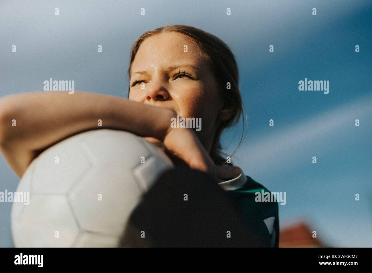 Kontemplatives Elementarmädchen mit Sportball, das gegen den Himmel blickt Stockfoto