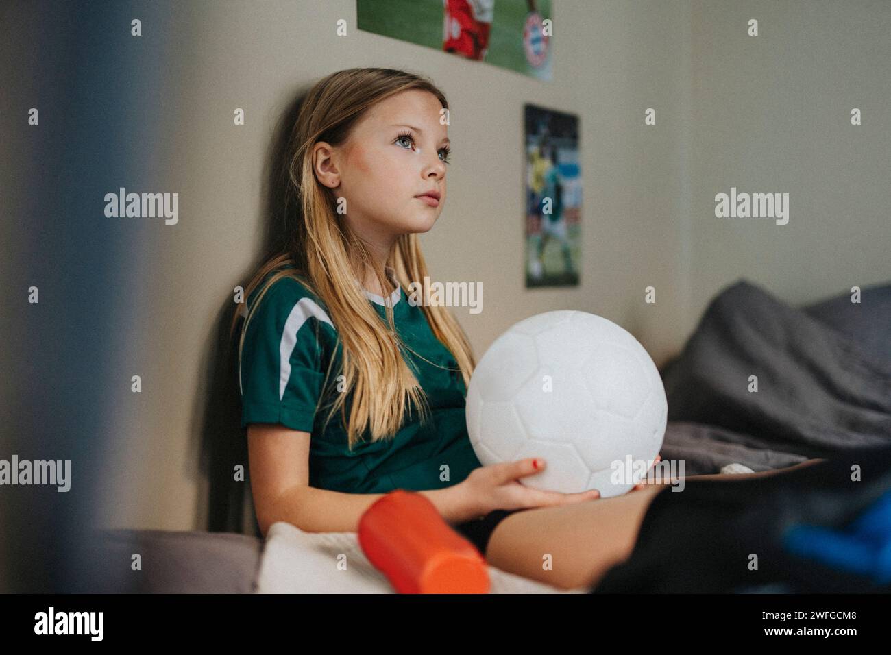 Grundmädchen mit Fußballtag träumt, während er zu Hause auf dem Bett sitzt Stockfoto