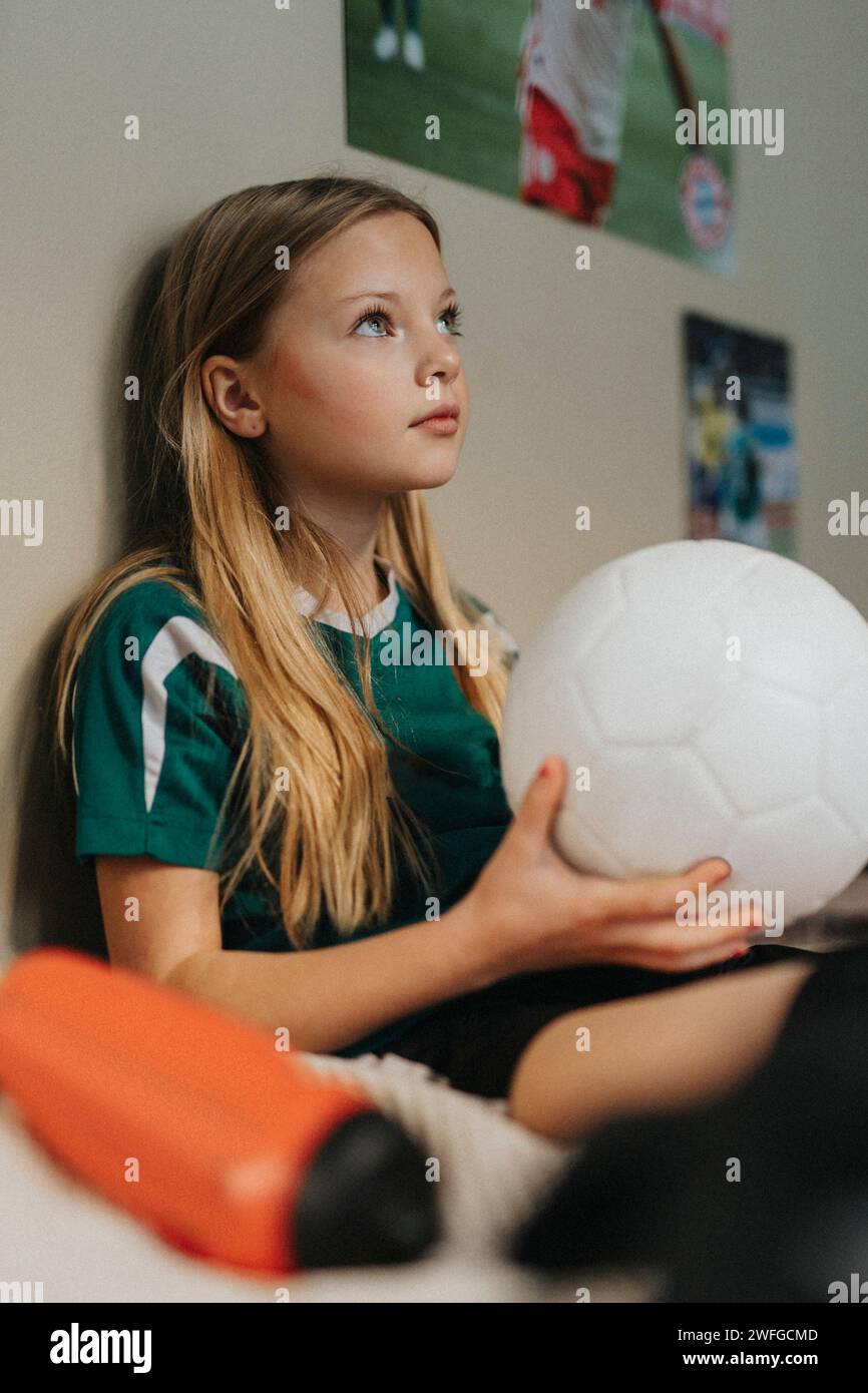Grundmädchen mit Fußball, das im Schlafzimmer sitzt Stockfoto