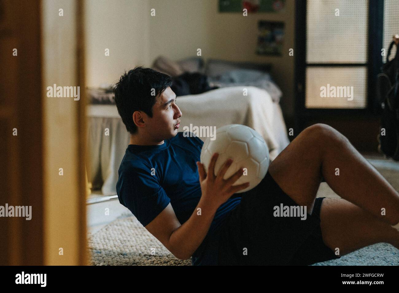 Ehrgeiziger Teenager mit Fußball, der zu Hause im Schlafzimmer sitzt Stockfoto