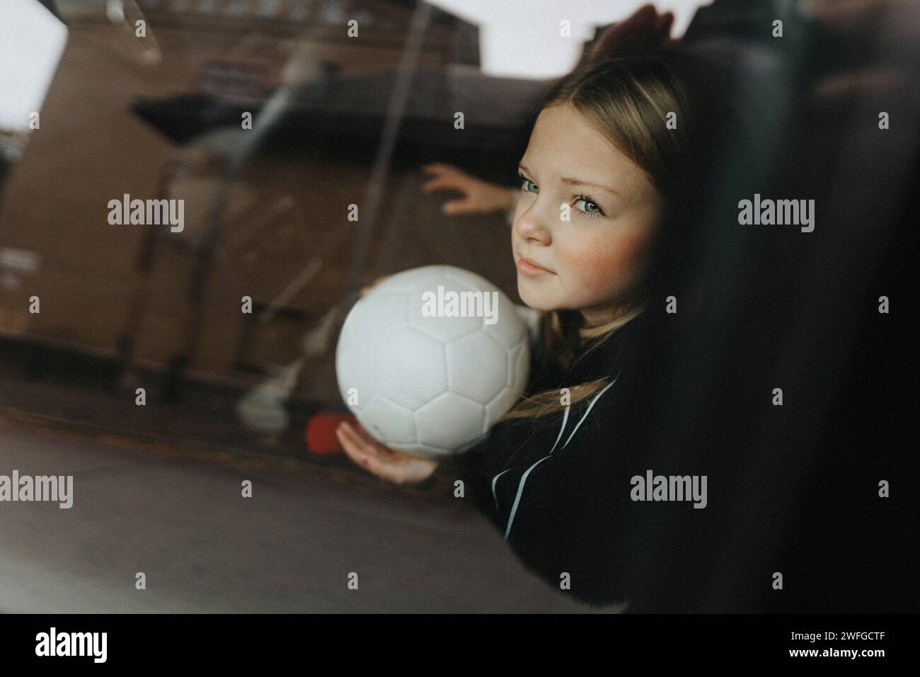 Besinnliches Mädchen mit Fußball durch ein Glas Auto gesehen Stockfoto