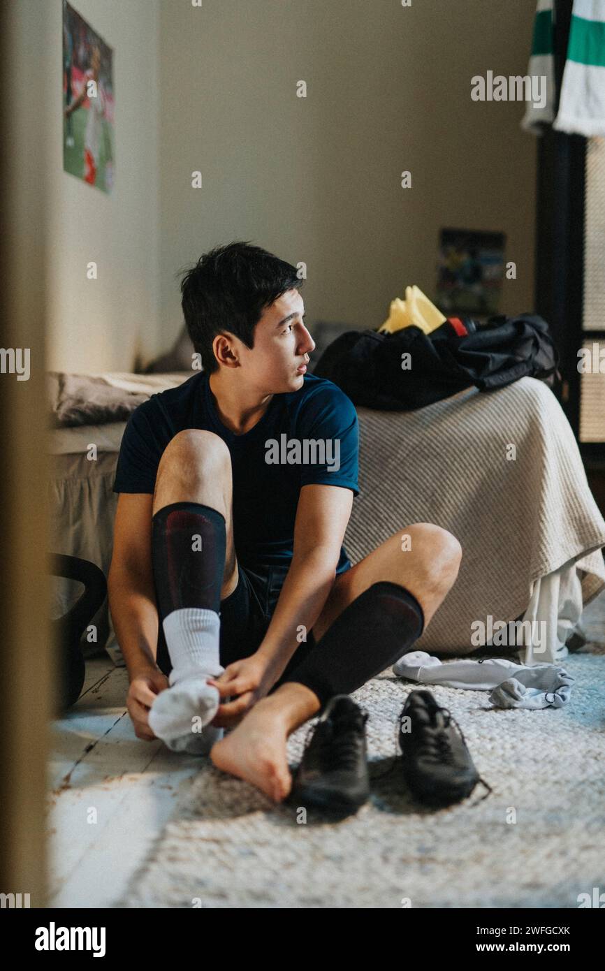 Teenager, der Socken trägt, während er zu Hause auf dem Boden sitzt Stockfoto