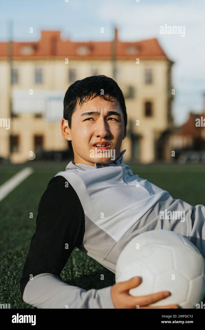 Männlicher Teenager-Athlet mit Fußball, der auf dem Sportplatz wegschaut Stockfoto