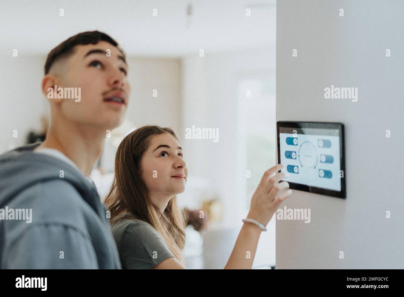 Geschwister passen die Beleuchtung des Raumes über ein digitales Tablet in einem modernen Zuhause an Stockfoto